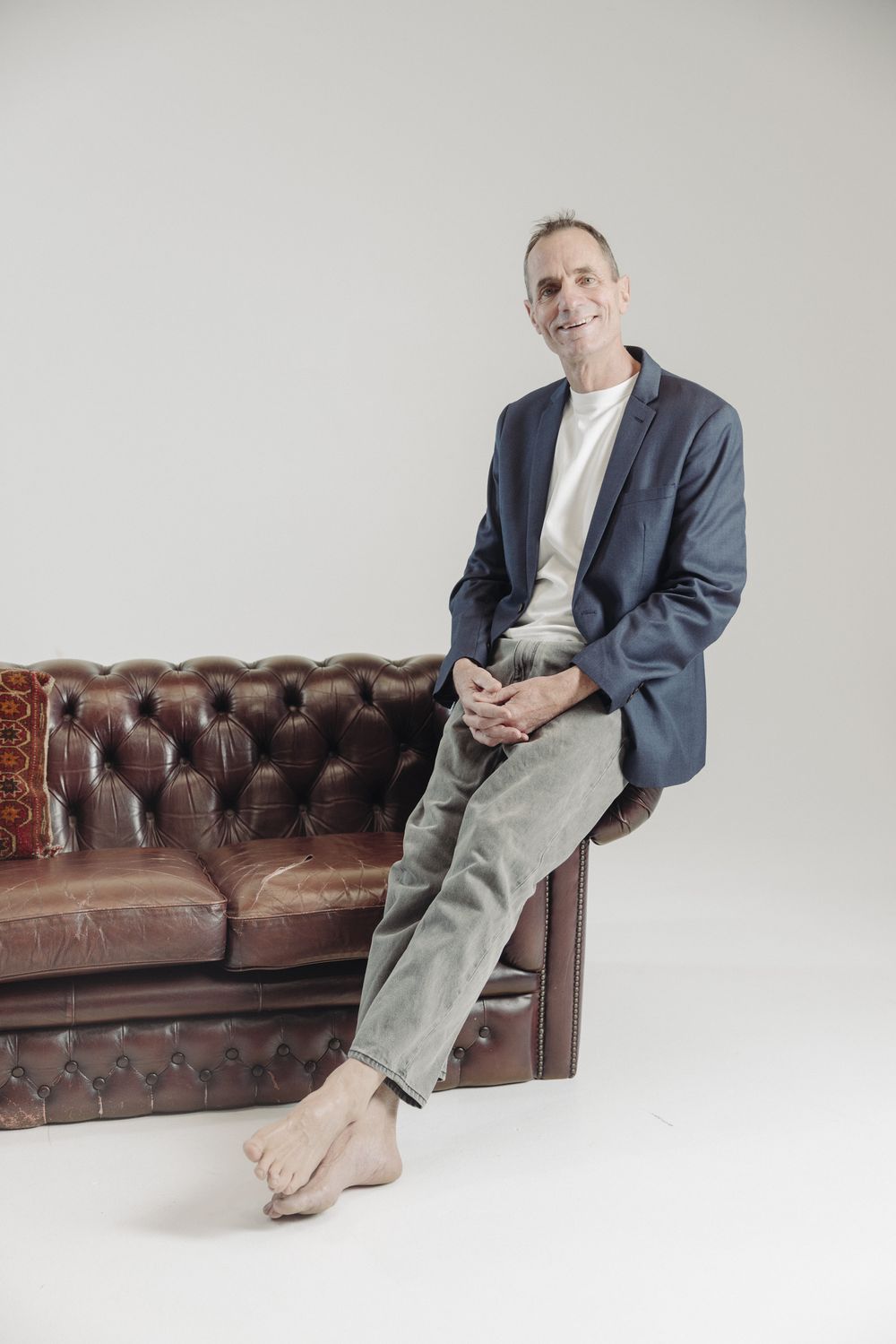 Mike Hunt sitting on the arm of a leather Chesterfield couch, smiling